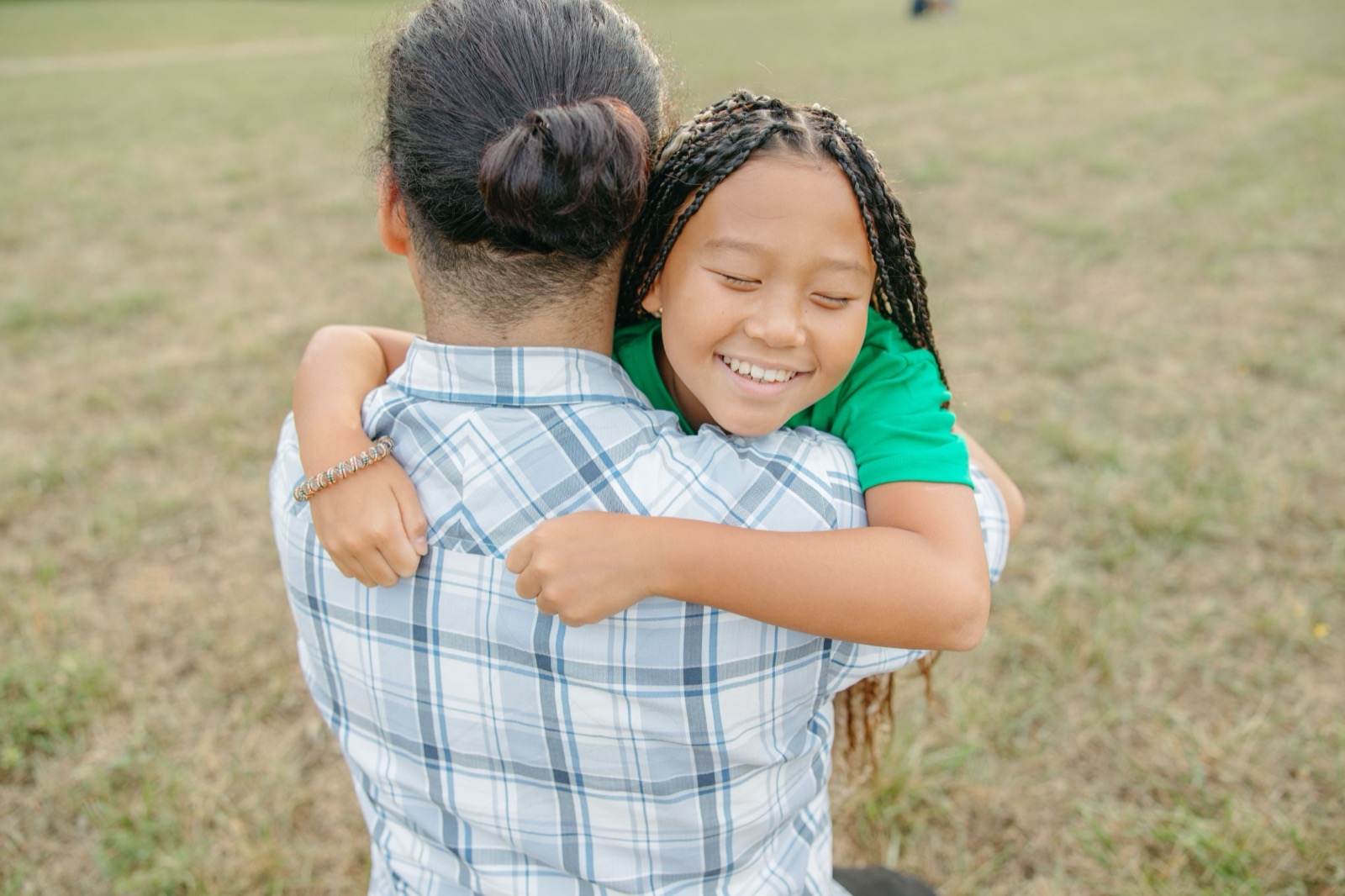Father and daughter share a warm embrace in a grassy field, capturing a moment of joy and bonding.
