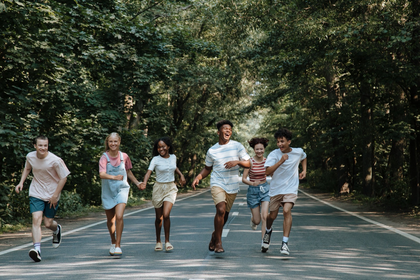 Group of joyful teenagers running and laughing on a forest road during summer.